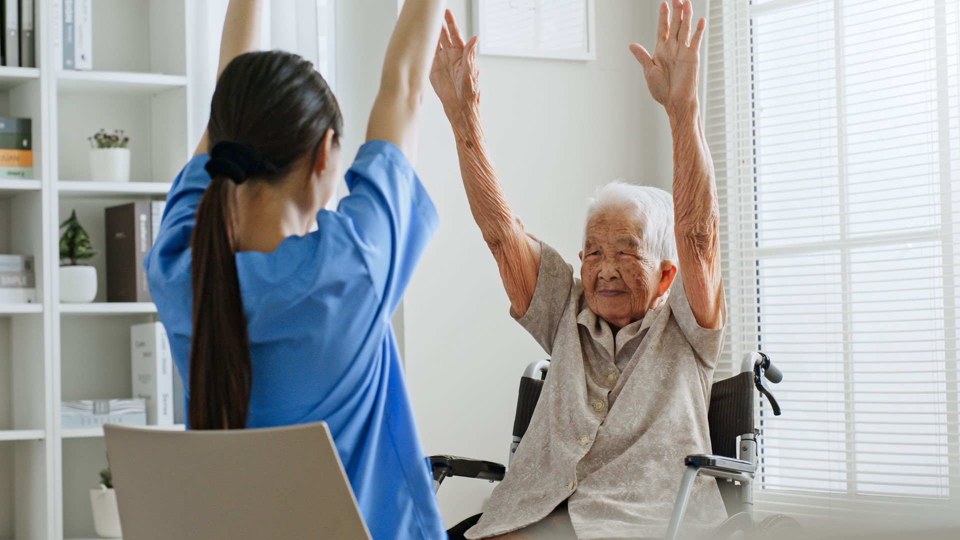 Young Asian woman nurse, caregiver assist a senior Asian woman to do physical therapy and exercise arms at home