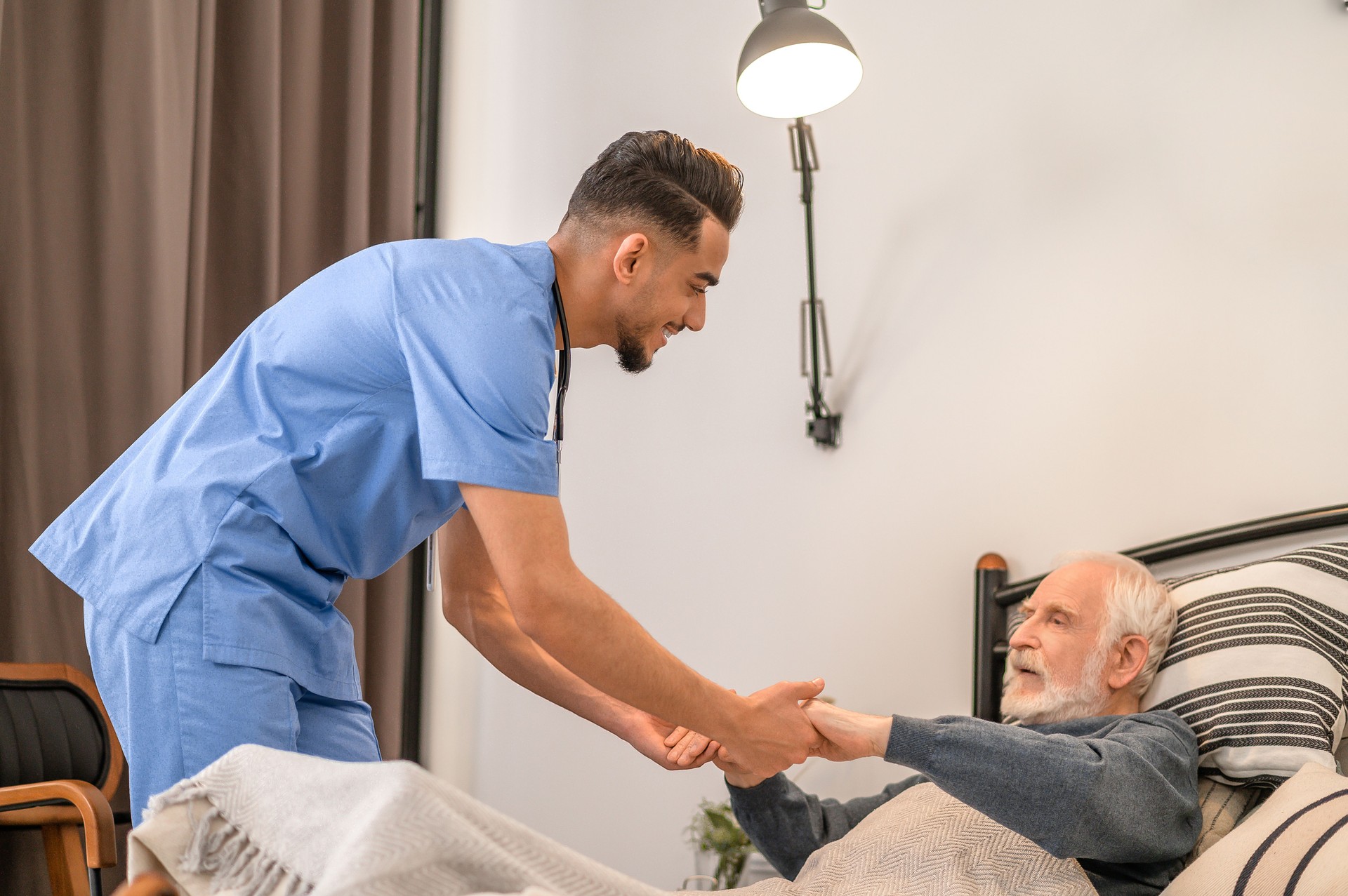 Smiling medical worker lifting the old man from the bed