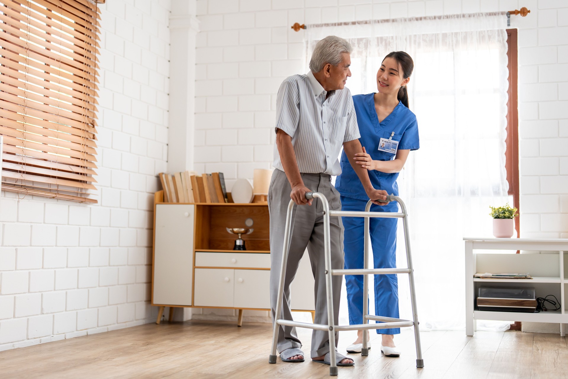 Asian senior elderly man patient doing physical therapy with caregiver. Attractive specialist carer women help and support older mature male practice walking slowly with walker at nursing home care.